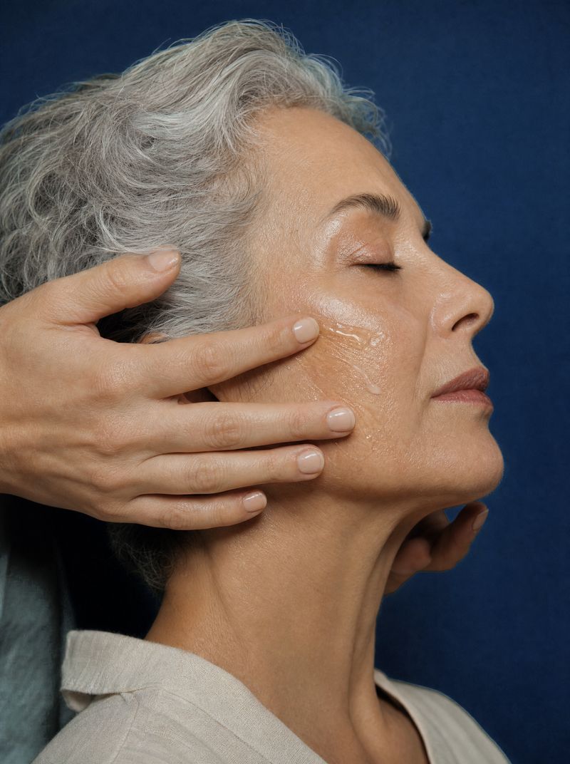 Esthetician smoothing serum along a client’s cheekbone